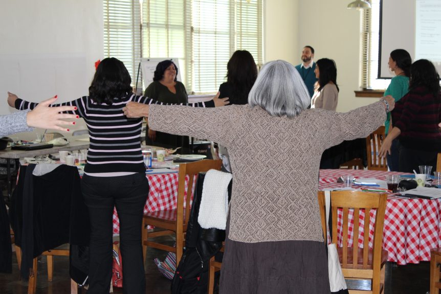 Participants of small gathering standing with arms outstretched and smiling.