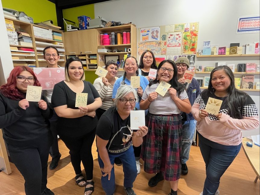 A group of people at a Risolana community workshop hold up their work for the camera.